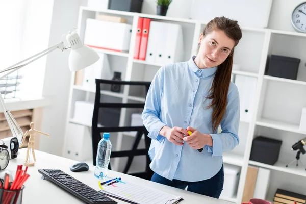 A young girl in the office is standing near the table and holding a yellow marker in her hand. — Stock Photo, Image