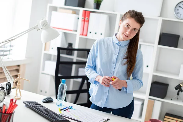 Een jong meisje in het kantoor is permanent in de buurt van de tafel ingedrukt te houden een gele markering in haar hand. — Stockfoto