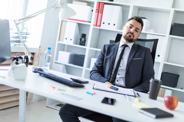 Bir adam masada ofiste bir sandalyede oturuyor.