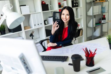 Koltuk beyaz masa ofiste oturan ve iyi işaret gösteren güzel genç kız.