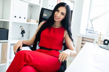 Kırmızı elbiseli güzel genç kız ofiste bir sandalyede oturuyor.