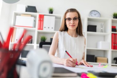 Güzel genç kız ofiste masada oturmuş, elinde kalem tutan ve belgeleri doldurma.
