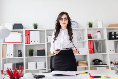 Güzel bir genç kız bir Ofis Masası duruyor ve onun elinde bir levha notları ve bir kalem için tutar.