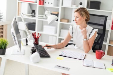 Genç sarışın kız ofiste bilgisayar masasında oturur, onun elinde bir kalem tutan ve klavyede yazdırır.