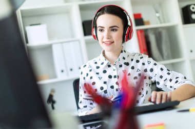 Güzel genç kız kulaklık Office masada oturur, onun elinde bir defter tutan ve klavyede yazdırır. Alan, kız odak derinliği ile fotoğraf.