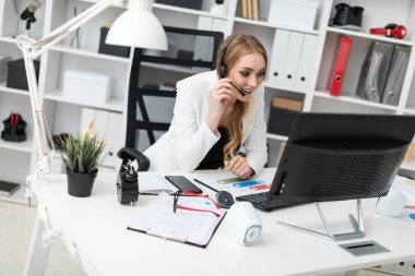 Kulaklık bir mikrofon ile genç bir kız ofiste bir masada oturur ve ekrana görünüyor.