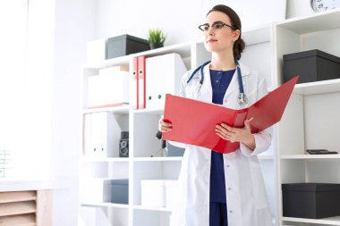 Güzel bir genç kız beyaz bir elbise içinde belgili tanımlık sığınak yakın duruyor ve belgeler ile kırmızı bir klasör üzerinden çevirir.