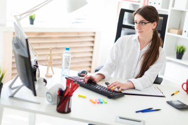 Genç bir kız ofiste bir masada oturan ve klavyede yazarak.