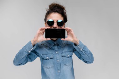 Yuvarlak gözlüklü genç esmer kız. Kıllar bir topuz toplanmış bulunuyoruz. Siyah bir telefon olan kız. Kız onun yüz bir telefon ile kaplı.