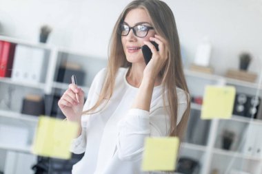 Genç bir kız şeffaf bir tahta sopa ile yakın duruyor ve onun elinde kalem tutan ve telefonda konuşuyor.