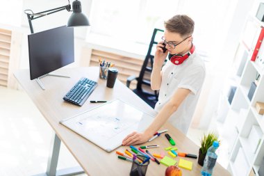Gözlüklü genç bir adam bir bilgisayar masası duruyor ve telefonda konuşuyor. Önce onu bir manyetik kurulu ve işaretleri yatıyor. Çocuklar kulaklık boynuna asmak.