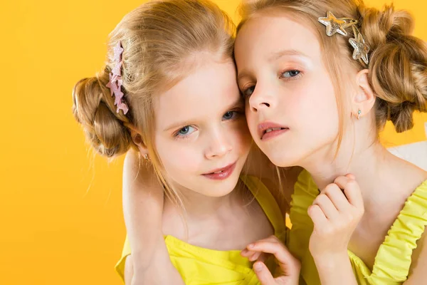 Дівчата-близнюки сидять на стільці на жовтому тлі . — стокове фото