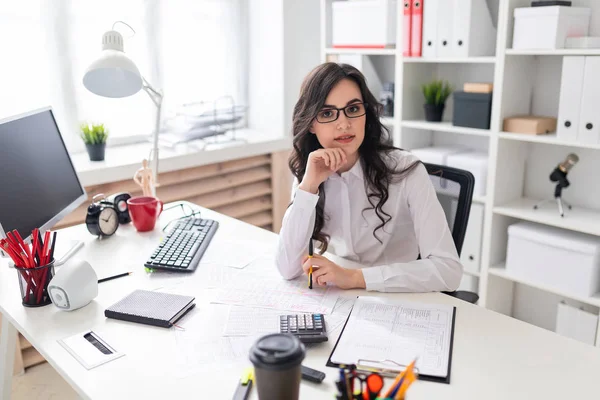 Een jong meisje zit aan de tafel van office en een pen in haar linkerhand houdt. — Stockfoto