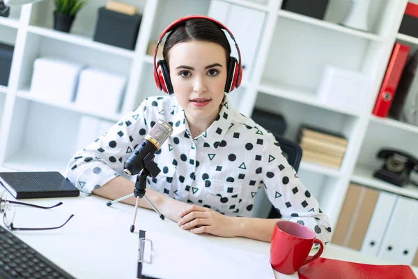 Güzel genç kız kulaklık bir mikrofon ofis masasında oturmuş.