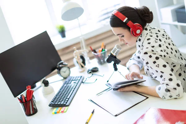 Mooi meisje zit in de koptelefoon en met een Kladblok aan de tafel in het kantoor en in de microfoon spreekt. — Stockfoto