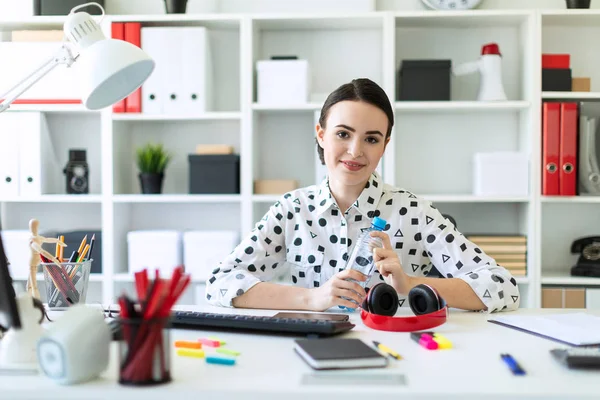 Een mooi jong meisje zit aan een tafel in het kantoor en een fles water houdt in haar handen. — Stockfoto