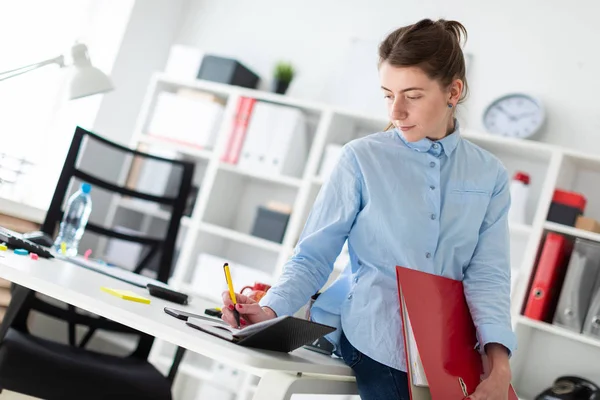 Una joven en la oficina está de pie, apoyada en una mesa, y escribiendo en un diario . — Foto de Stock