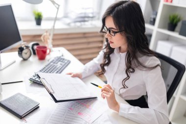 Genç bir kız ofis masada oturur ve belgeleri denetler.