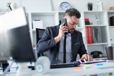 Bir adam telefonda konuşurken ve belgeleri ve bir hesap makinesi ile çalışma masasında ofisinde oturuyor.
