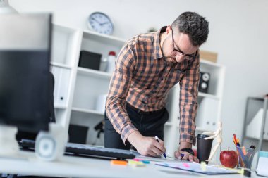Bir adam ofiste masanın yanında duruyor ve bir işaretleyici manyetik tahtaya çizer.