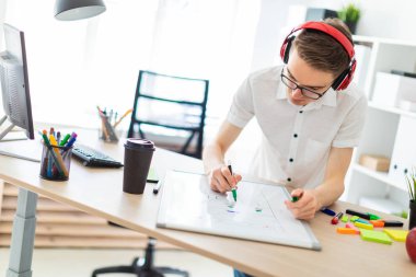 Gözlüklü ve kulaklıklı genç bir adam manyetik tahtaya bir işaret çizer..