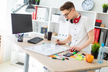 Gözlüklü genç bir adam bir bilgisayar masası duruyor. Genç bir adam bir işaretleyici manyetik bir tahtaya çizer. Çocuklar kulaklık boynuna asmak.