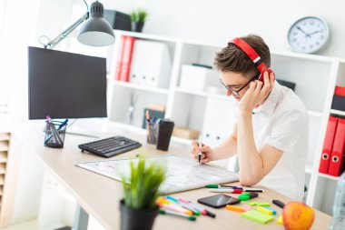 Bir genç adam gözlük ve kulaklık bir bilgisayar masası duruyor. Genç bir adam bir işaretleyici manyetik bir tahtaya çizer..