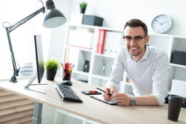 Gözlüklü genç bir adam ofiste bir tabloda yakınındaki standları ve elinde bir kalem tutar.