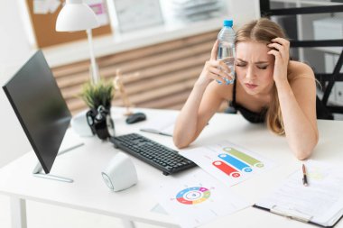 Genç bir kız ofiste bilgisayar masasında oturur ve bir şişe su kafasına koyar.