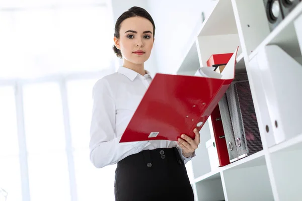 Ung flicka på kontoret nära rack och bläddrar igenom mappen med dokument. — Stockfoto