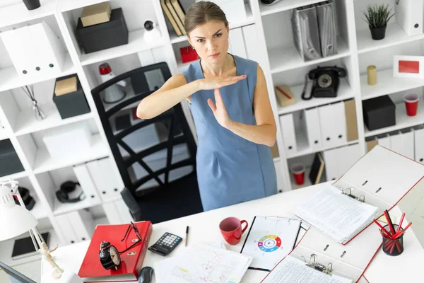 Ein junges Mädchen steht an einem Tisch im Büro und hält eine Handfläche senkrecht zur zweiten. — Stockfoto