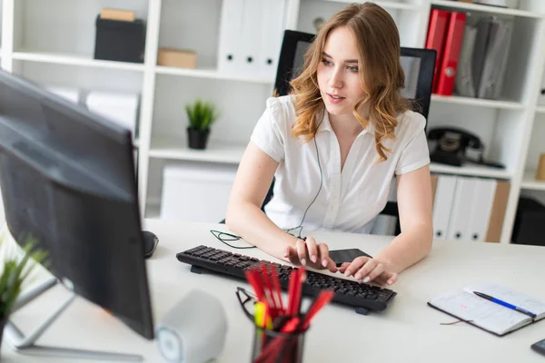 Mooi jong meisje werken met de computer in kantoor. Het meisje heeft een luidspreker en een telefoon voor haar. — Stockfoto