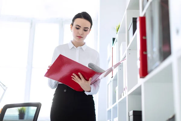 Ung flicka på kontoret nära rack och bläddrar igenom mappen med dokument. — Stockfoto