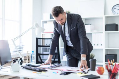Adam ofiste standları, ellerini masanın üstüne koyar ve belgeler görünüyor.