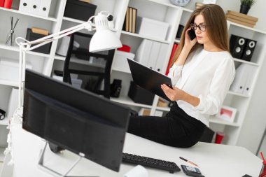 Genç kız ofiste, tabloda bir tablet sayfalarıyla birlikte onun elinde tutan ve telefonda konuşurken oturdu.