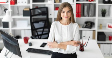 Genç bir kız ofiste bir tabloda yaslanmış ve gözlük onun elinde tutan duruyor.