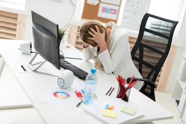 Una joven está sentada en una mesa en la oficina y cogida de la mano detrás de su cabeza. . — Foto de Stock