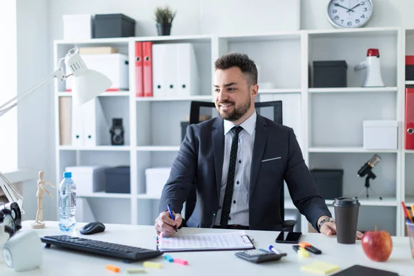 Ein Mann sitzt im Büro am Tisch, hält ein Glas Kaffee und einen Stift in der Hand und arbeitet mit Dokumenten. — Stockfoto