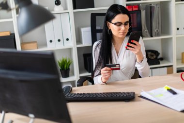Genç bir kız bir banka kartı ve telefon tutarak masada oturuyor.