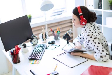 Güzel genç kız kulaklık ve bir not defteri ofiste masada oturur ve mikrofona konuşur.