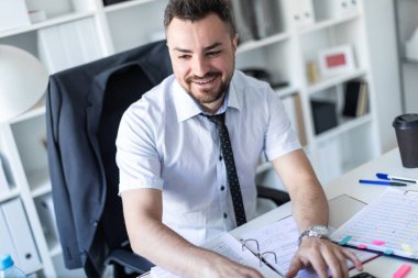 Bir adam belgeleri ve bir bilgisayar ile çalışma ofisinde, bir masada oturuyor.