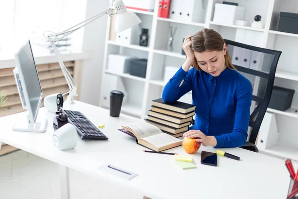 Uma menina senta-se em uma mesa de computador e segura a mão na cabeça. Antes da menina encontra-se um livro aberto e uma maçã . — Fotografia de Stock