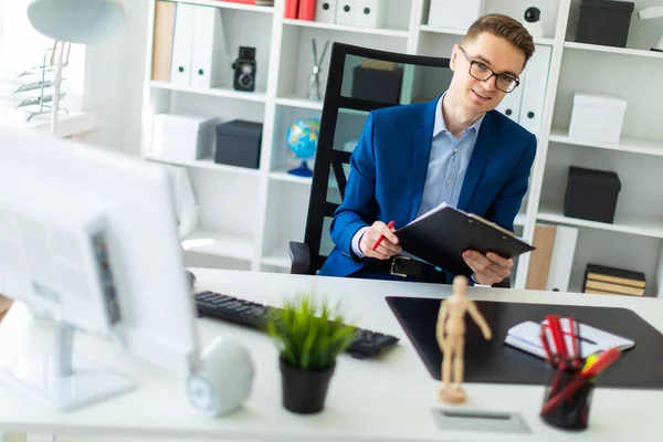 Ein junger Mann sitzt an einem Tisch im Büro und hält Dokumente und Stift in den Händen. — Stockfoto