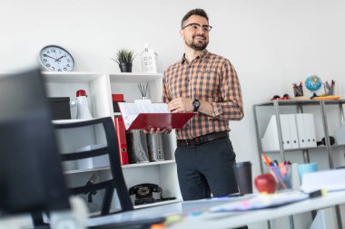 Ofiste bir adam raf standları ve belgeler klasörüyle üzerinden kaydırır.
