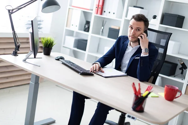 Ein junger Mann sitzt im Büro am Tisch, telefoniert und hält einen Bleistift in der Hand. Der junge Mann hat Dokumente. — Stockfoto