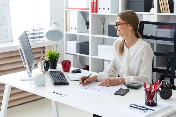 Genç bir kız ofiste bilgisayar masasında oturur ve onun elinde kalem tutan.