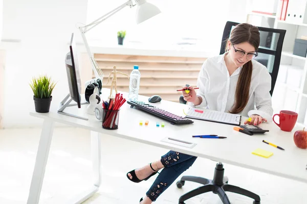 En ung flicka sitter vid ett bord på kontoret, håller en penna i sin hand, en markör och räknar på en miniräknare. — Stockfoto