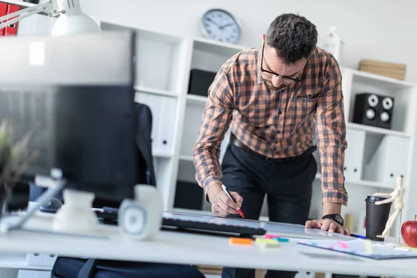 Bir adam ofiste masanın yanında duruyor ve bir işaretleyici manyetik tahtaya çizer.