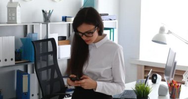 Smartphone kullanarak ve modern ofis kamerada içine gülümseyen iş kadını