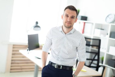 Genç bir adam ofiste bir masaya yaslanmış duruyor..